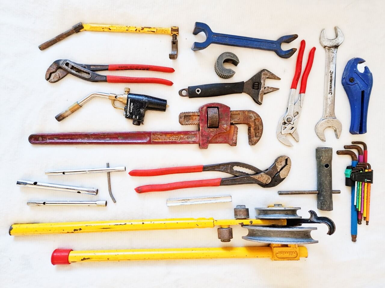 a flat lay of plumbing tools including wrenches and a pipe bender, used across the AK Plumbing London blog
